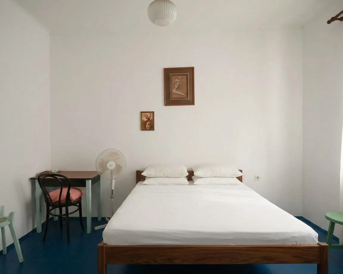 Double bedroom with white linen, a small desk and a fan