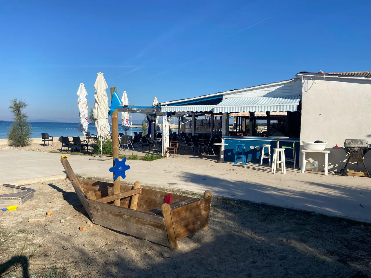 Beach bar with umbrellas and a wooden boat sandpit for children on Olib
