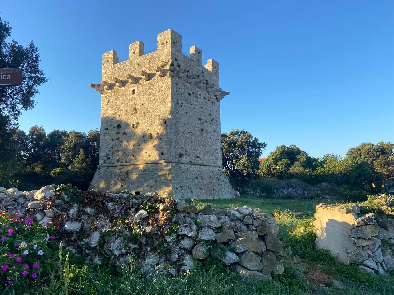 The square stone Kula defence tower with battlements, surrounded by greenery